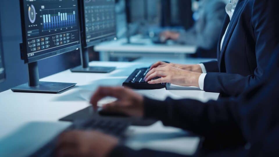 Close Up Hands Shot of a Technical Support Specialist of Software Engineer Working on a Computer in a Dark Monitoring and Control Room. He types on Keyboard and Moves the Mouse.